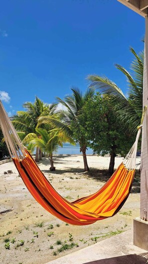 A hammock on a concrete platform with a view of a beach and palm trees. - Birdhouses Hummingbird is a very unique place in the sunset side of the island. (Caye Caulker.)