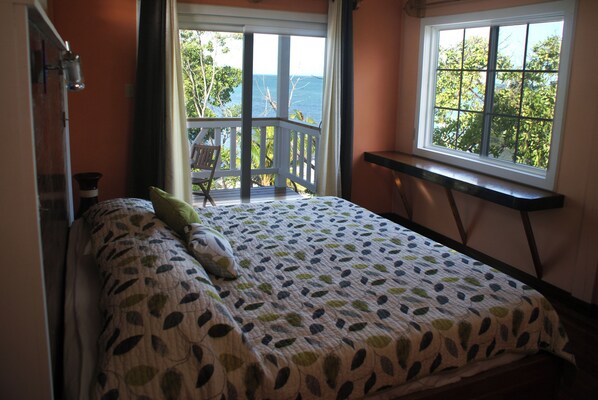 A bedroom with a bed, a window with a view of the outdoors, and a small table. - Birdhouses Hummingbird is a very unique place in the sunset side of the island. (Caye Caulker.)