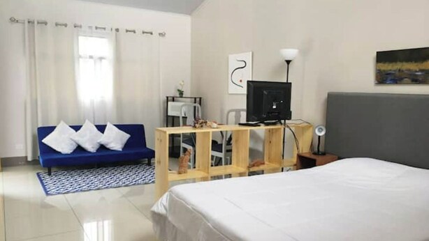 A hotel room with a bed, a desk with a computer, a blue sofa, and a window with curtains.