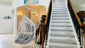 Un interior amplio con una escalera, una silla colgante y un comedor.