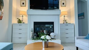 Una sala de estar moderna con chimenea, muebles blancos y un televisor de pantalla plana montado encima.