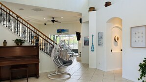 Un interior espacioso con una escalera de madera, un sillón colgante y un piano.