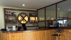 A bar area with a wooden counter, shelves with bottles, and a large window. - Tiger Wildlife Resort (Jagatpur)