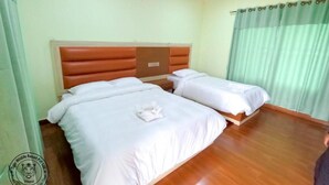 A hotel room with two beds, wooden flooring, and a green curtain. - Tiger Wildlife Resort (Jagatpur)