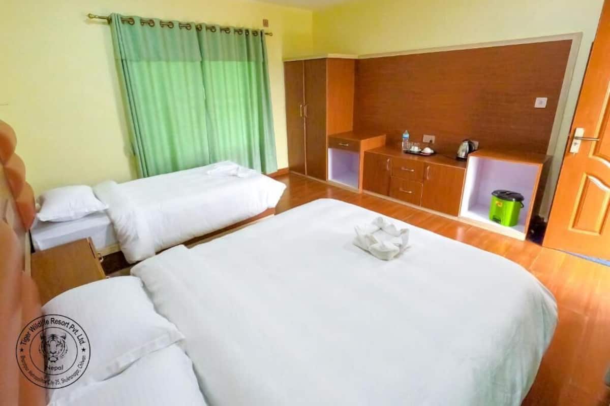 A hotel room with two beds, a wooden wardrobe, a green curtain, and a small kitchenette area.