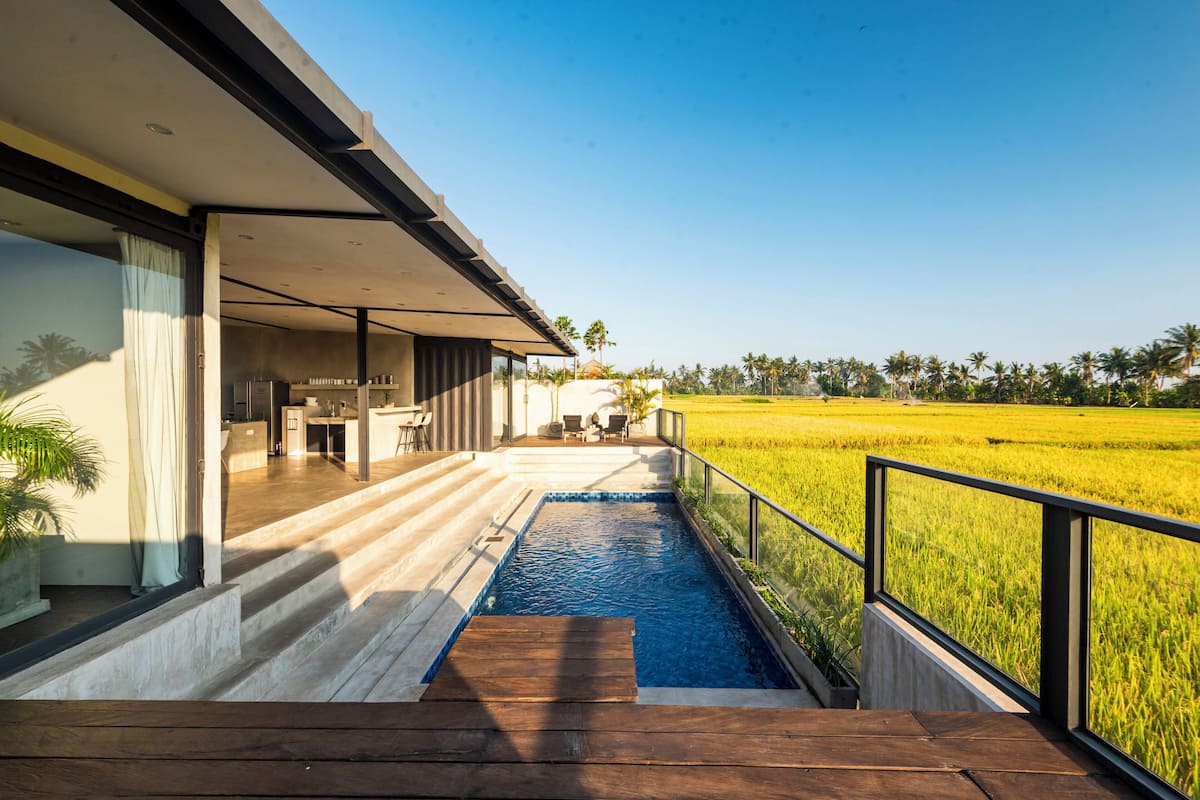 A modern house with a swimming pool, a patio, and a view of a rice field.