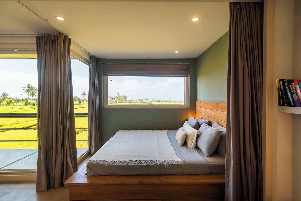 A bedroom with a large window, a bed, and a wooden headboard.