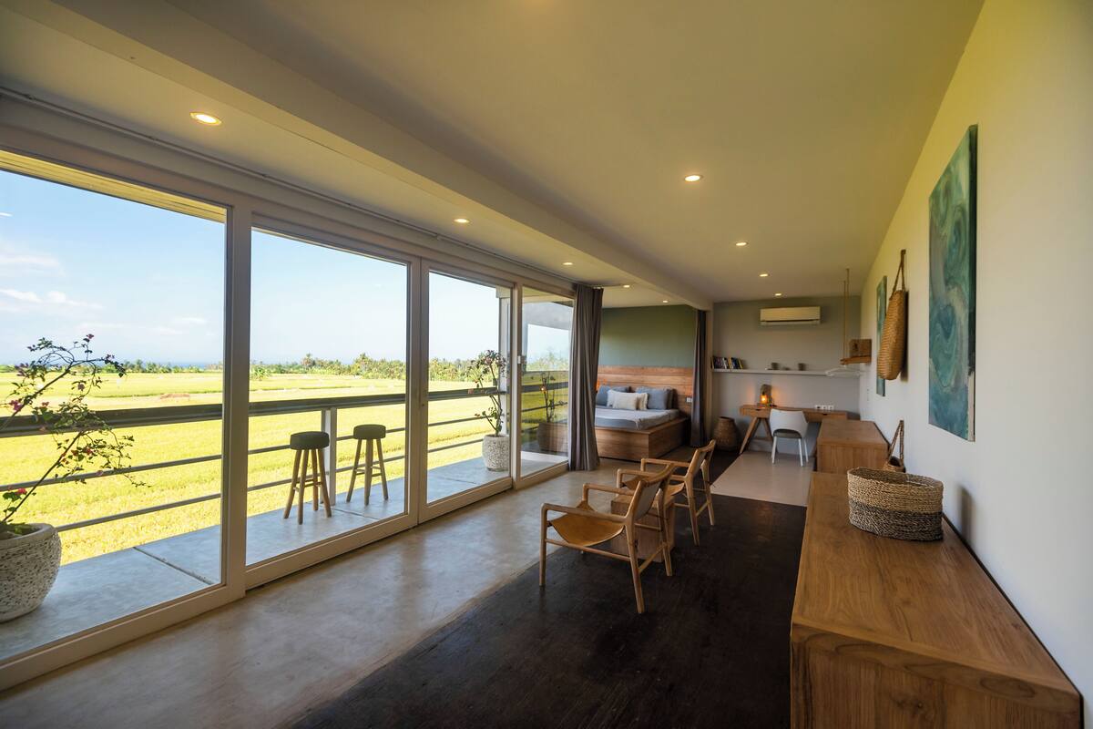 A spacious room with large windows, a wooden bench, a sofa, and a dining area.