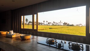 A kitchen with a large window overlooking a green field and palm trees. - Joshua District (Tabanan)