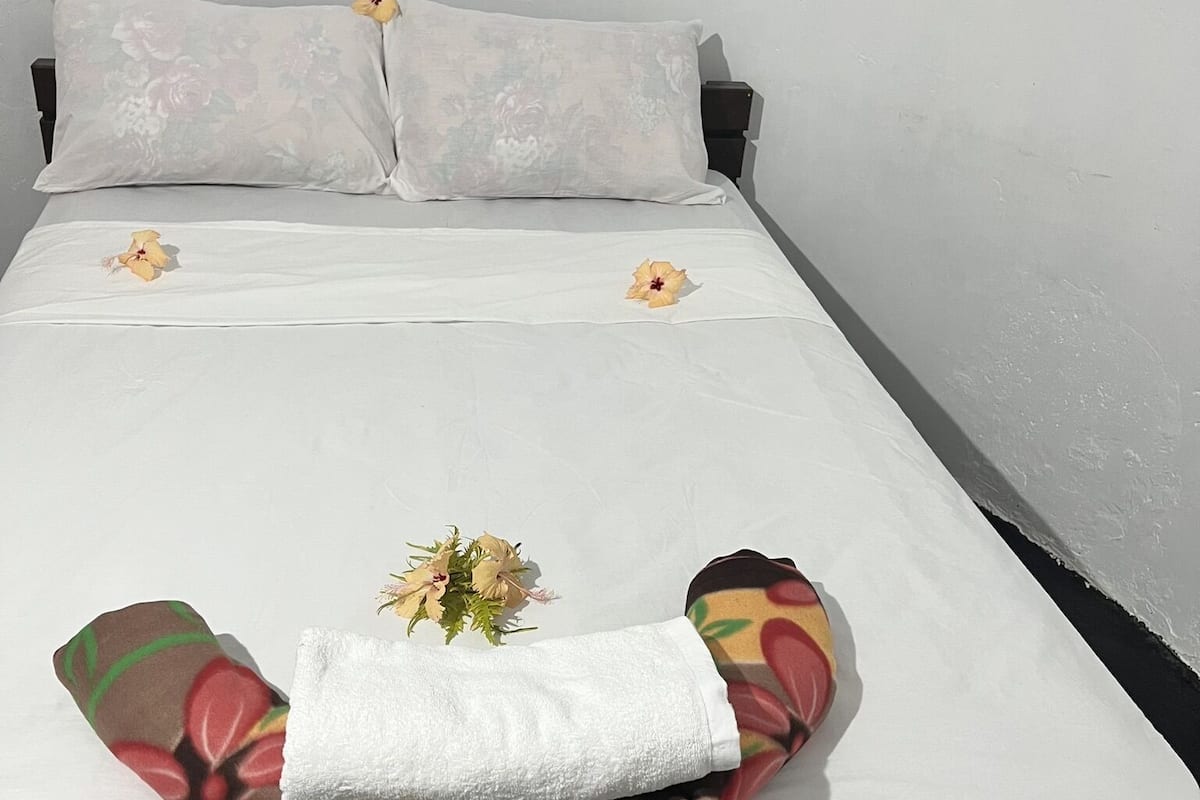 En snyggt bäddad säng med vita sängkläder, två dekorativa kuddar och en blomsteruppsättning på sängen.