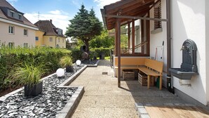 Une cour avec un banc en bois, un chemin de pierres et une plante en pot.