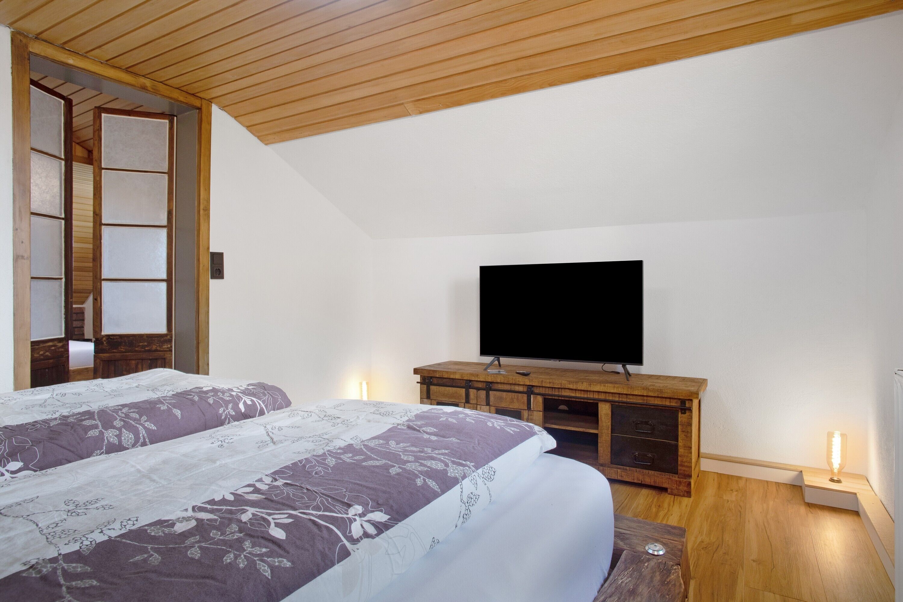 Une chambre à coucher avec un lit, un téléviseur posé sur un meuble en bois et une porte coulissante traditionnelle.