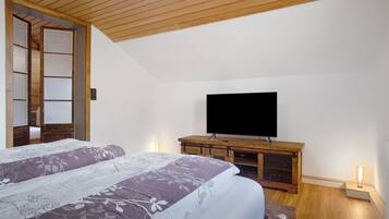 Une chambre à coucher avec un lit, un téléviseur posé sur un meuble en bois et une porte coulissante traditionnelle.