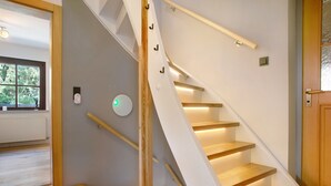 Un escalier moderne avec des marches en bois et une rampe blanche, menant à une pièce équipée d’un radiateur et d’une fenêtre.