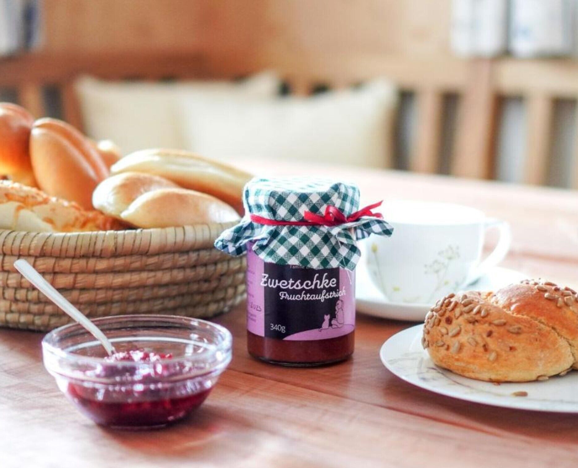 A table with a jar of Zwetschke fruit compote, a bowl of jam, and a basket of bread.