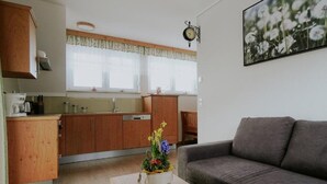 Una cocina moderna con armarios de madera, un rincón de comedor con sofá gris y un reloj fijado a la pared.