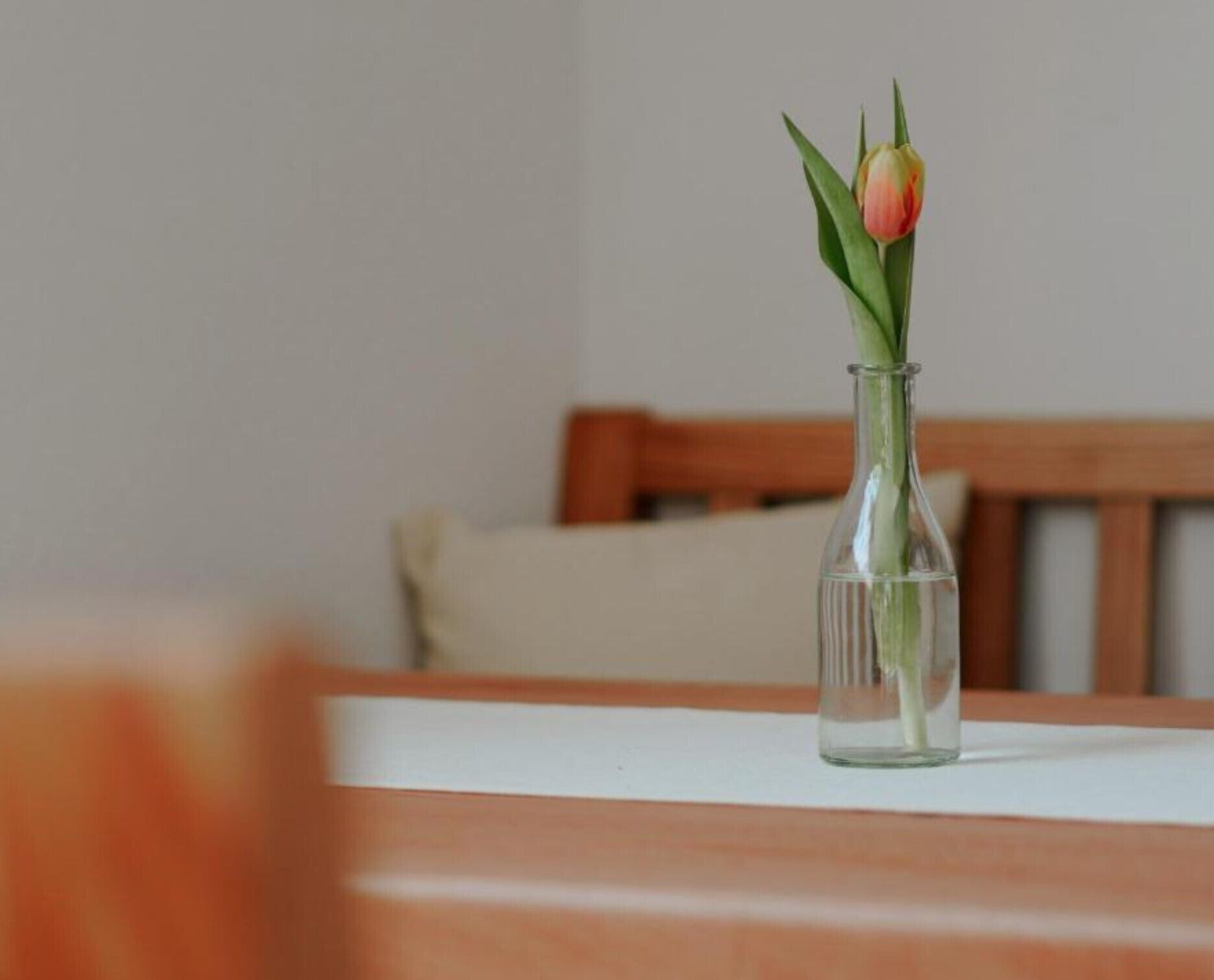 A clear glass vase with a single tulip on a wooden table.