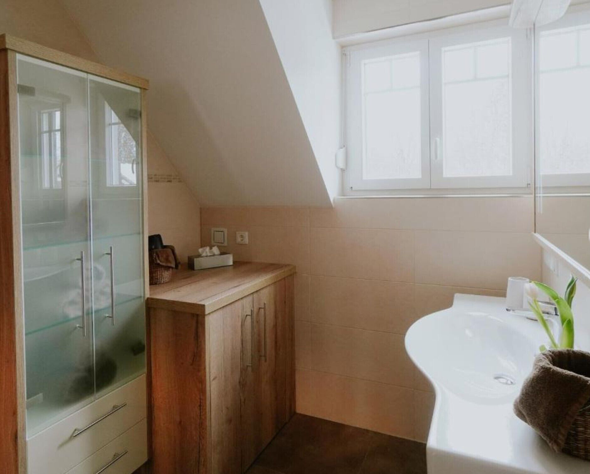 Ein Badezimmer mit Holzschrank, weißem Waschbecken und Fenster darüber.