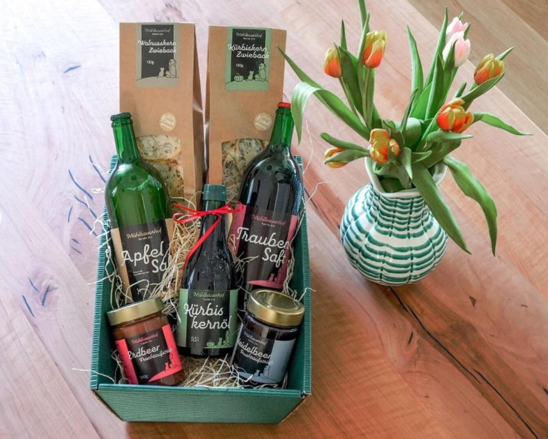 A gift basket with bottles and jars, a vase with tulips, and two boxes.