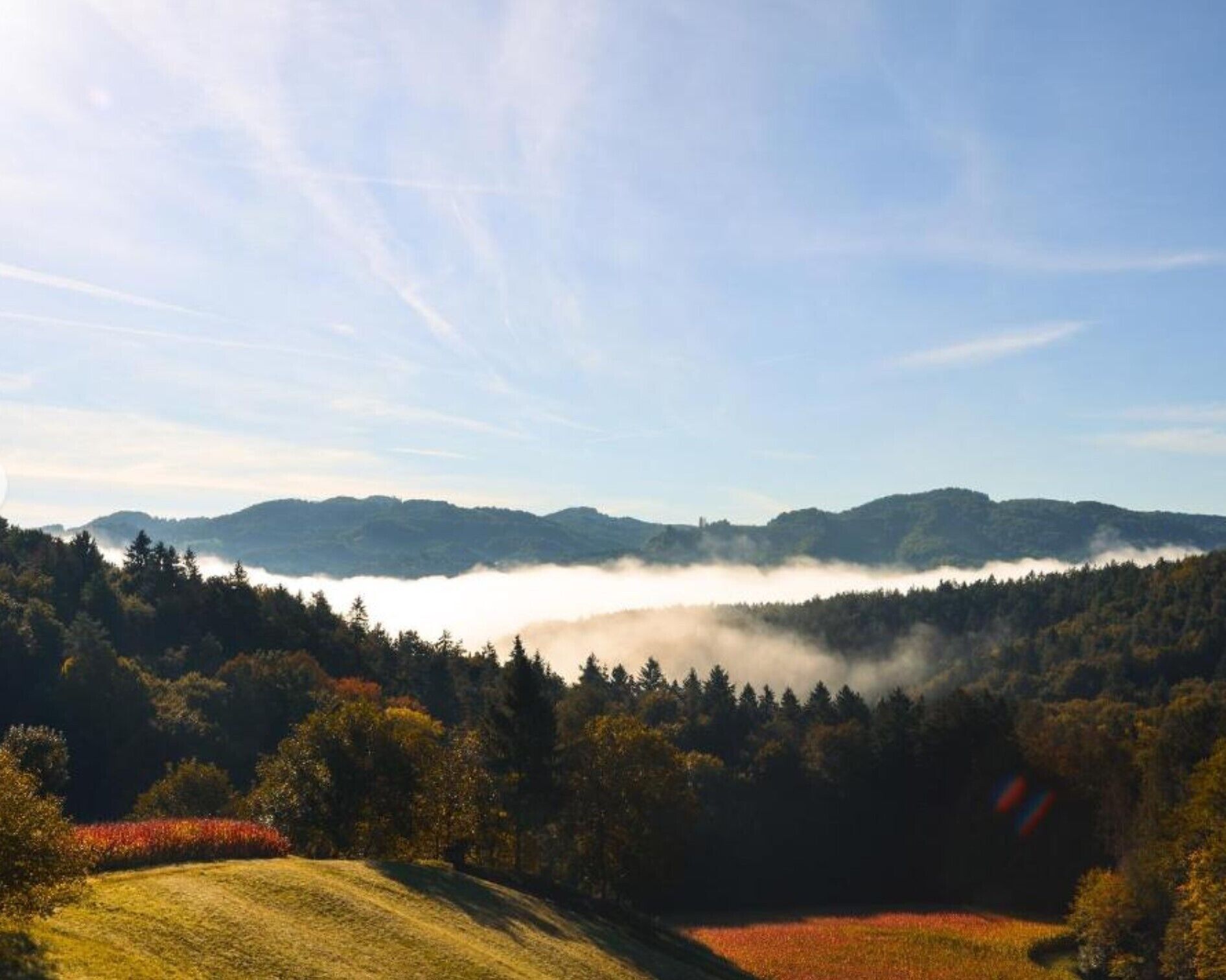 A mountainous landscape with a valley, forested hills, and a clear sky.
