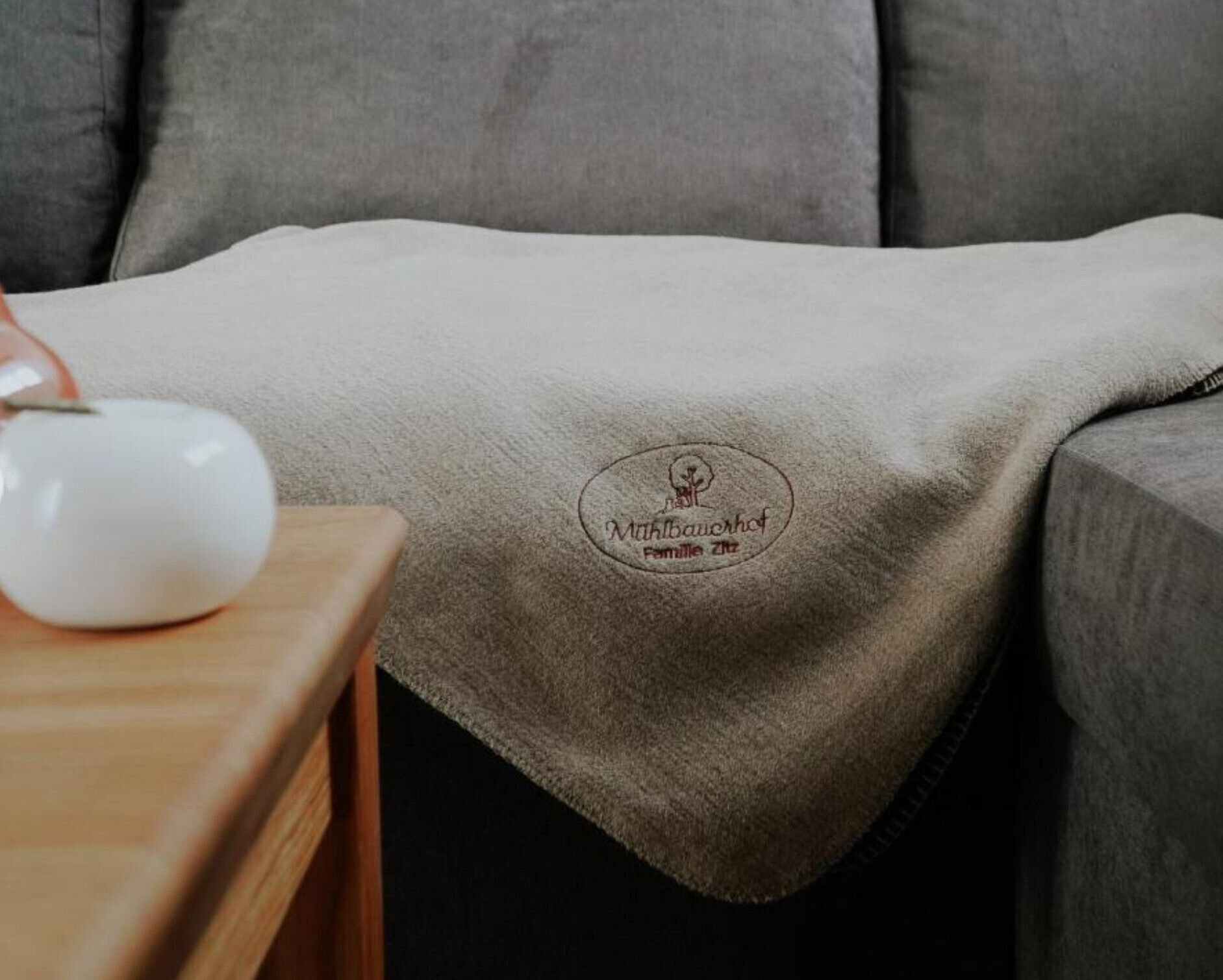 A grey sofa with a blanket featuring a logo and text.