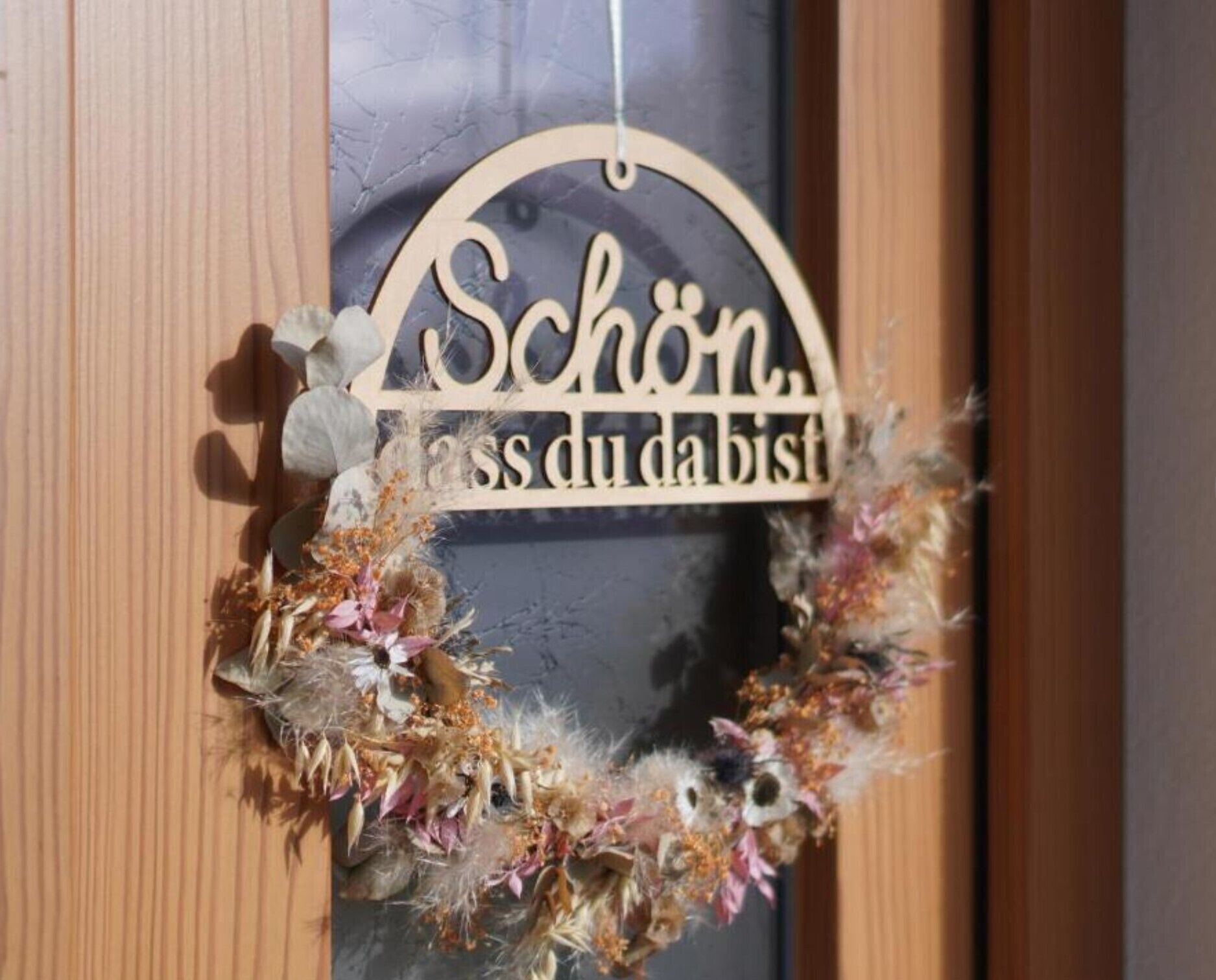 Une enseigne en bois portant l’inscription « Schön, lass du bist » et ornée d’une couronne décorative.