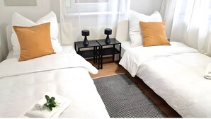 Une chambre d’hôtel avec deux lits, une petite table et une fenêtre avec des rideaux légers.