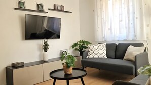 Un salon moderne avec un téléviseur à écran plat, un canapé, une table basse et deux plantes en pot.