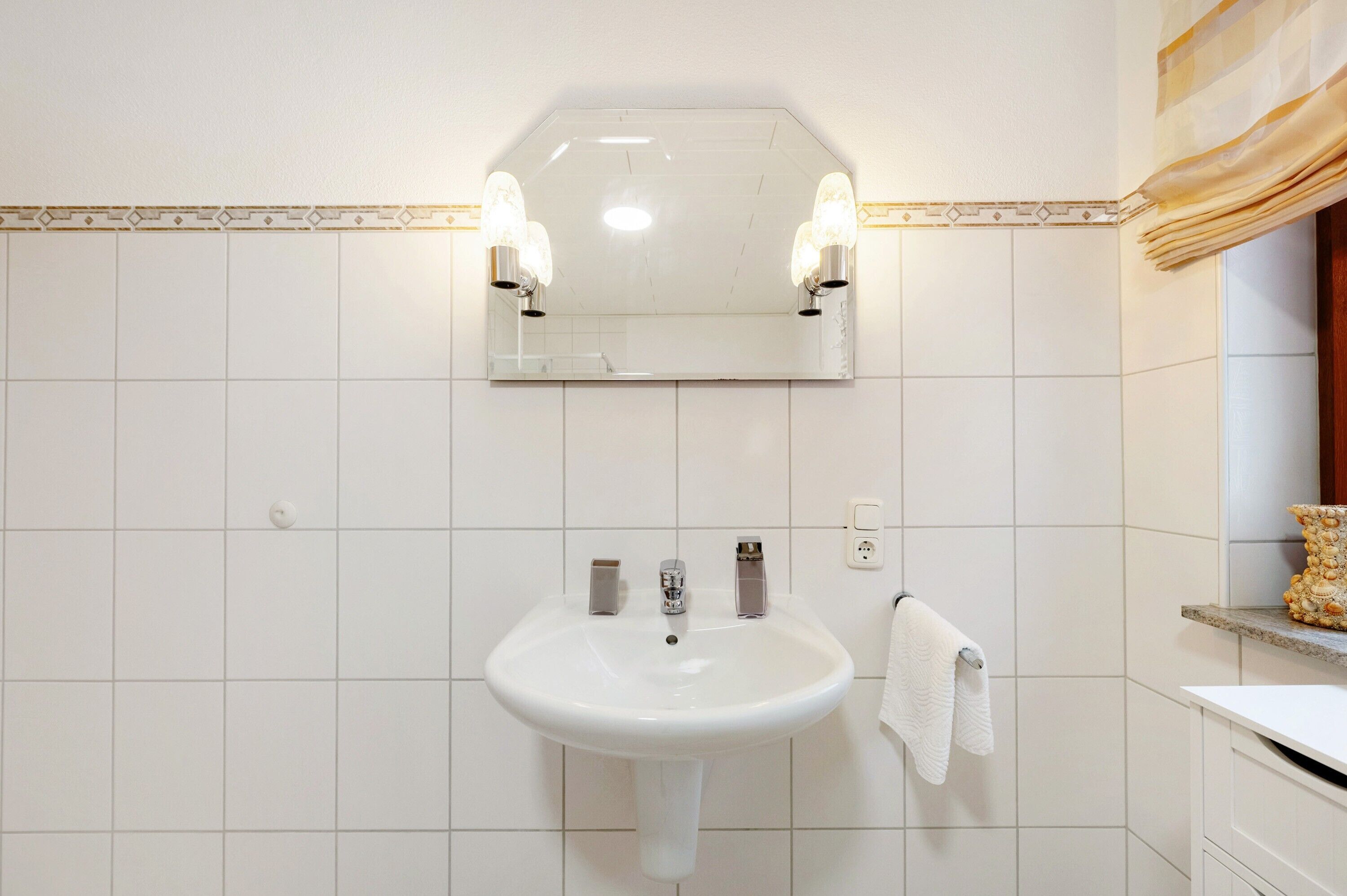 Un baño con lavamanos blanco, espejo y dos luces empotradas.