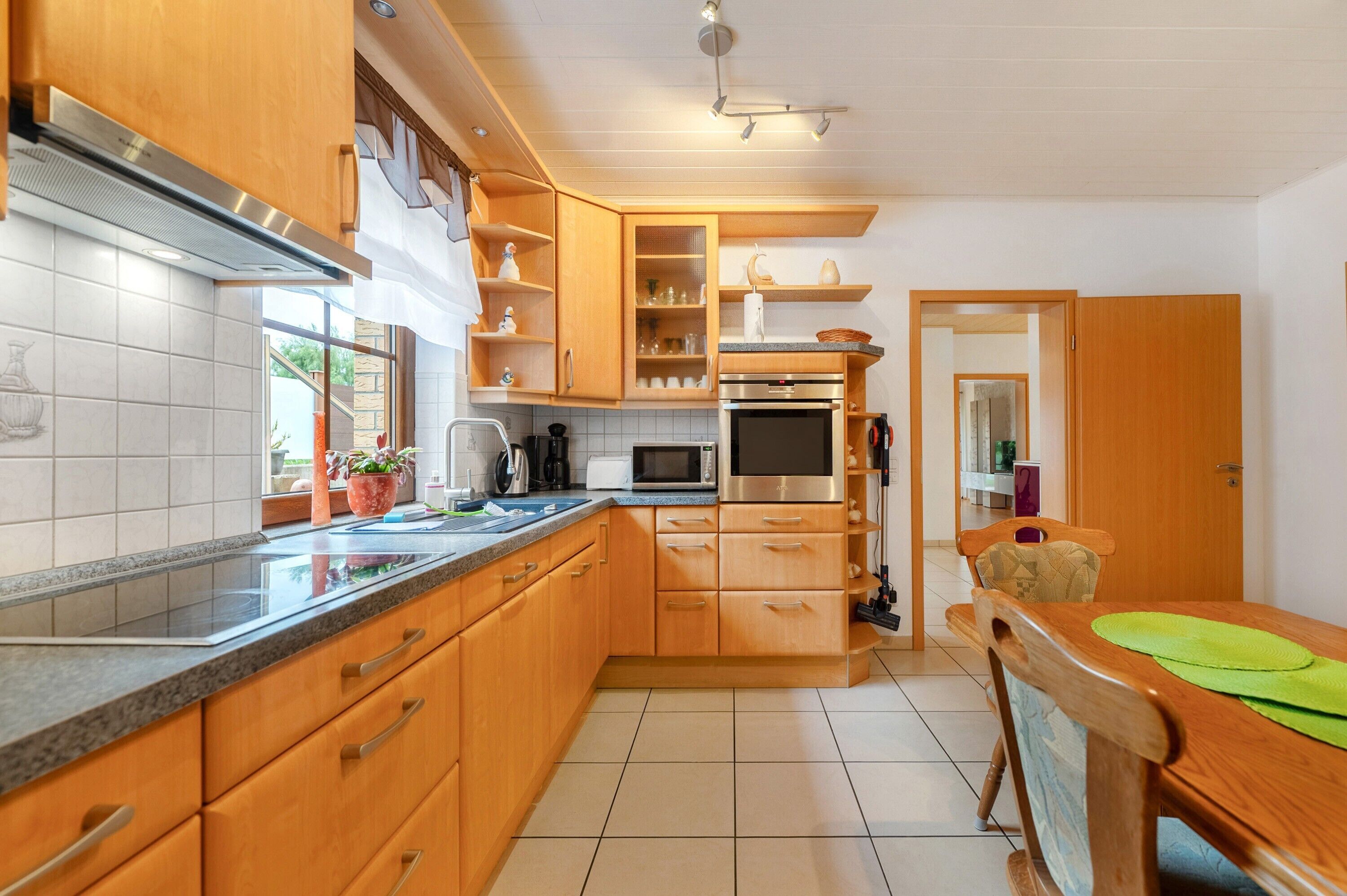 Una cocina con armarios de madera, microondas, horno y comedor con mesa y sillas.