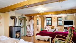 Ein gemütliches Zimmer mit Kamin, einer Couch, einem Fernseher und einer Holzbalkendecke.