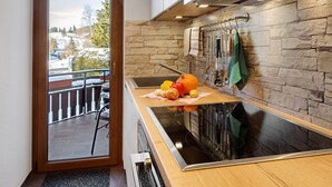A kitchen with a stone wall, a view of a snowy landscape, and a wooden table with kitchen utensils. - Apartment 'Oskar' with Garden View, 2 Balconies and Wi-Fi (Titisee-Neustadt)