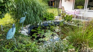 A garden with a pond, decorative birds, and a patio area with chairs and a table. - Holiday Apartment 'Eule' with Wi-Fi (Donaueschingen)