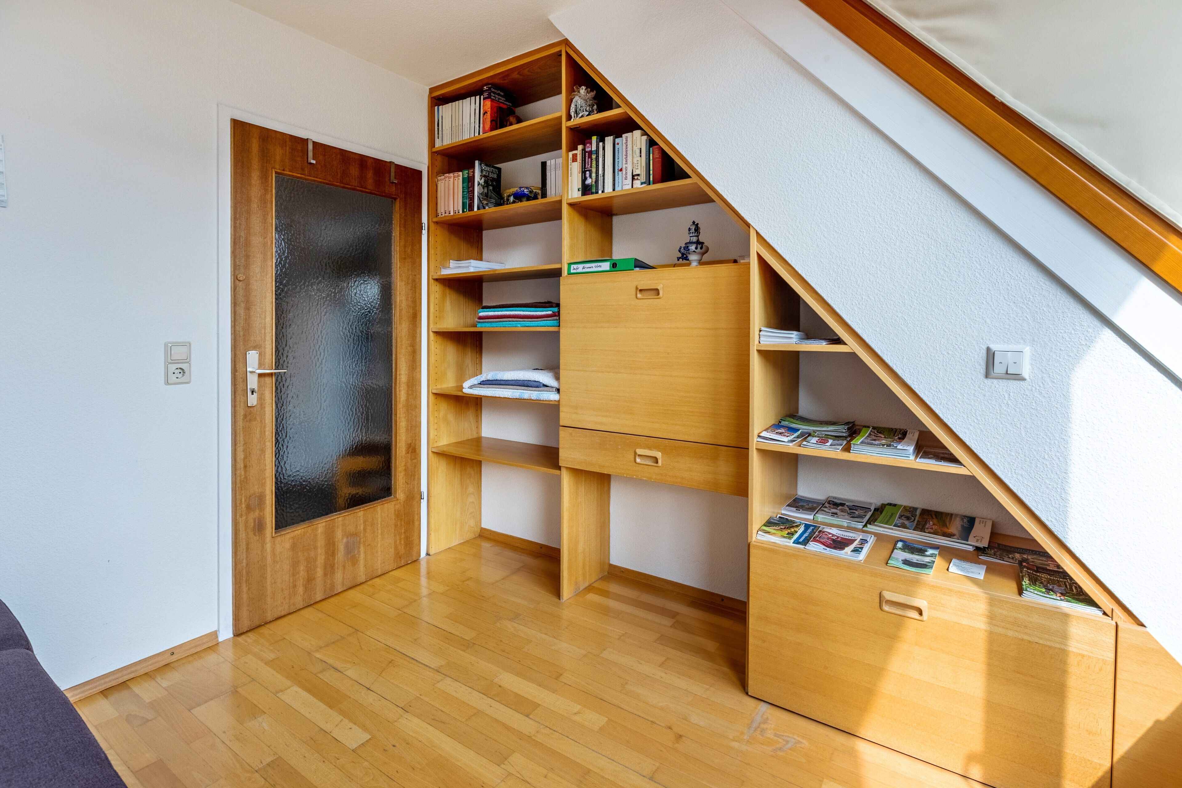 Habitació amb terra de fusta, una prestatgeria, escriptori i una porta.
