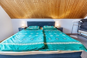 A bedroom with a wooden ceiling, a bed with teal bedding, two bedside tables with lamps, and a ladder against the wall.