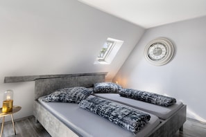 Une chambre à coucher moderne avec une lucarne, une horloge murale ronde et un lit agrémenté d’oreillers à motifs.