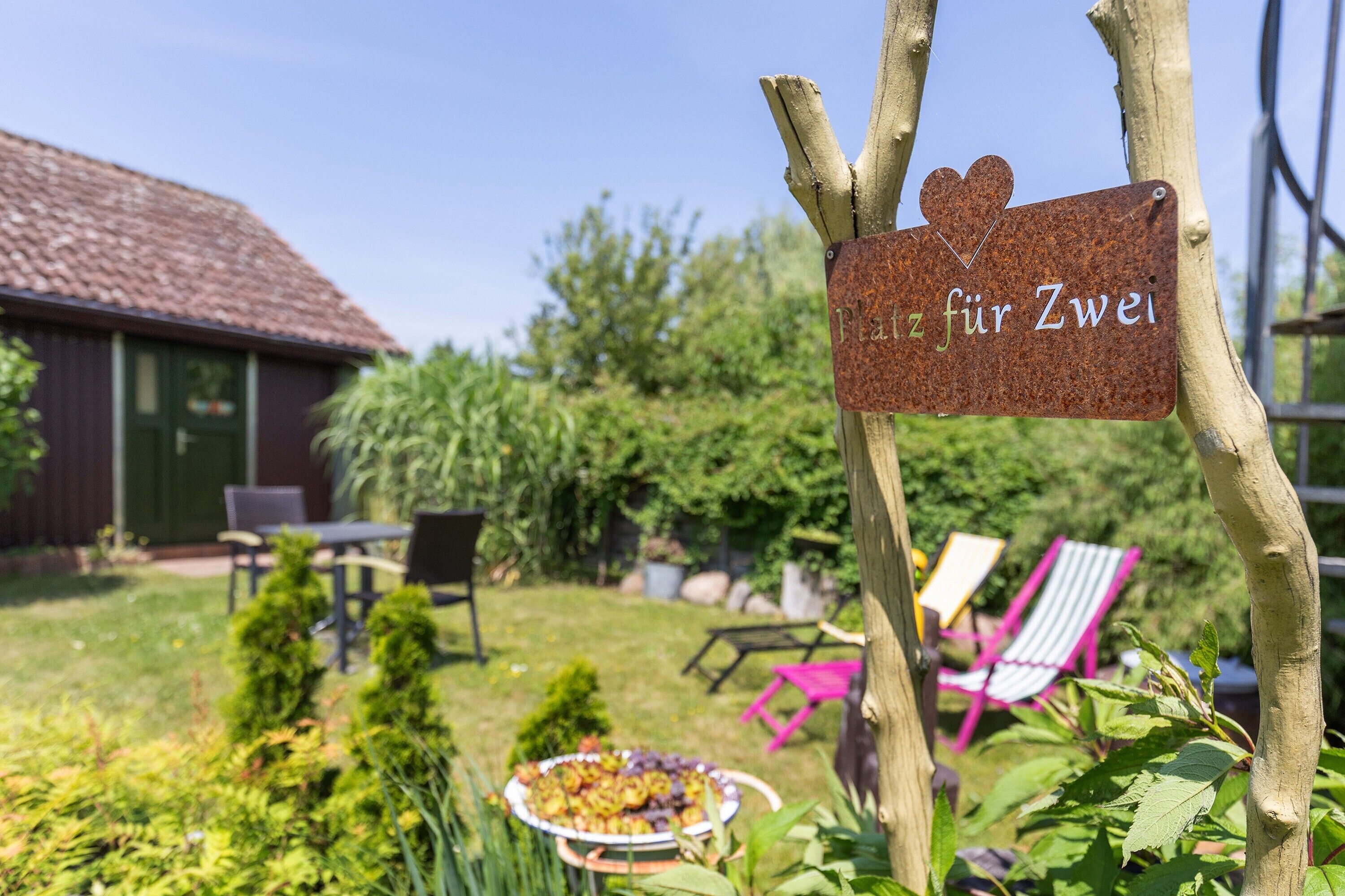 Ein rustikaler Außenbereich mit Holzschild, einem Esstisch mit einem Teller Essen und zwei bunten Stühlen.