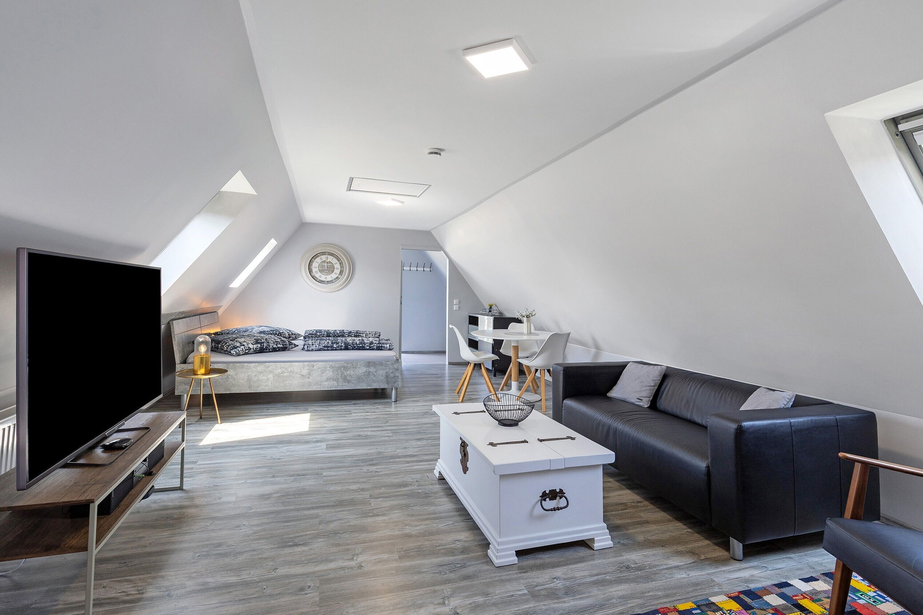 Una sala de estar moderna estilo loft con una televisión de pantalla plana, un sofá, una mesa de centro y una zona de comedor con sillas y una mesa.