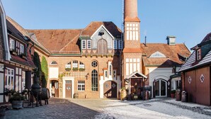 A historic building with a tall chimney, a cobblestone courtyard, and traditional architecture.
