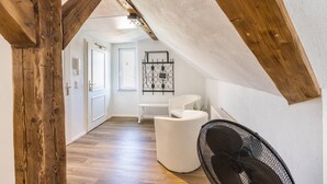 A loft-style room with exposed wooden beams, a white bench, a black chair, and a wall-mounted metal rack.