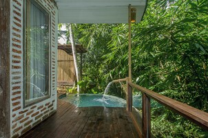 Terraza de madera con piscina, rodeada de abundante vegetación y una valla de bambú.