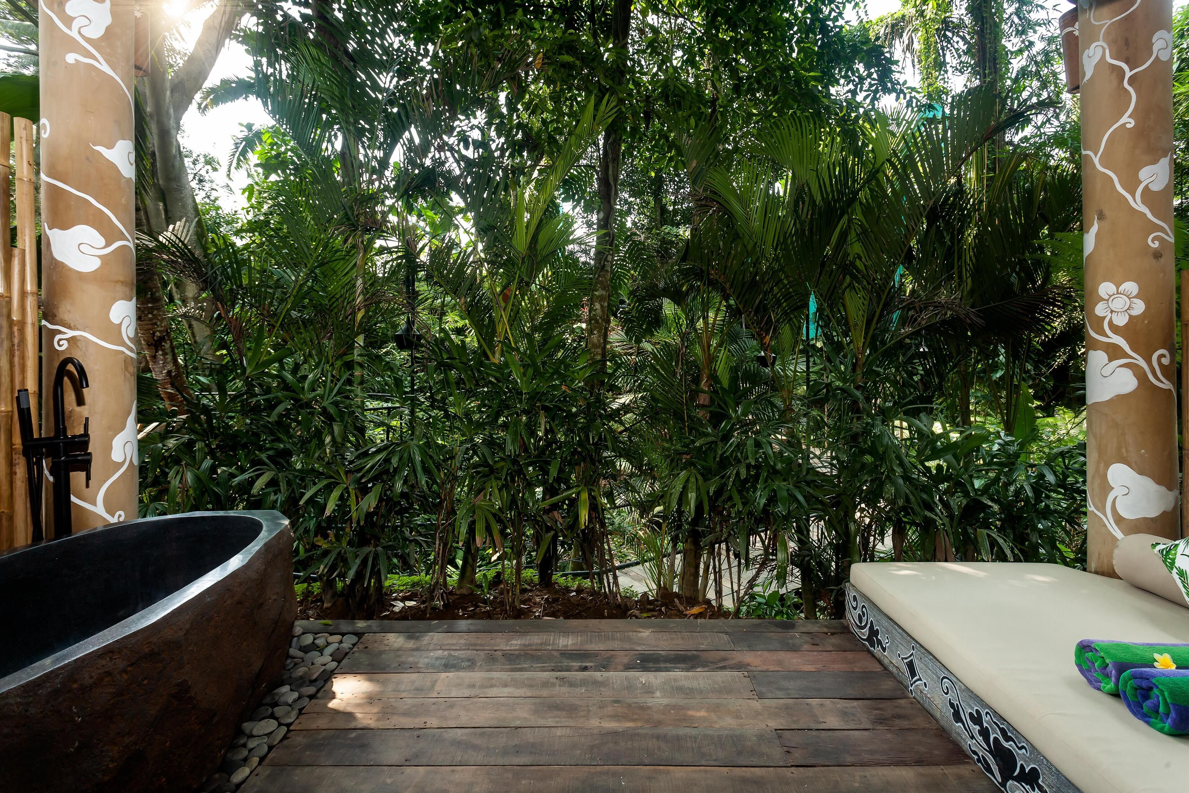 A wooden staircase leading to a room with a bathtub and a bed, surrounded by lush greenery.