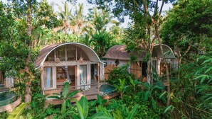 A rustic treehouse with a curved roof, surrounded by lush greenery and palm trees. - Sacred Canyon Ubud by GenuineHost (Payangan)