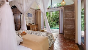 A bedroom with a canopy bed, a small table with a candle, and a view of a pool and greenery. - Sacred Canyon Ubud by GenuineHost (Payangan)