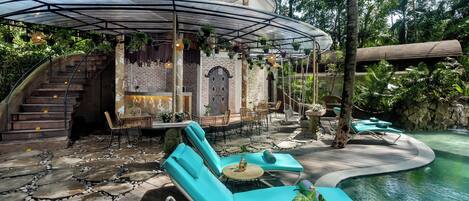 A circular outdoor seating area with lounge chairs and a small table, surrounded by a pool and lush greenery.