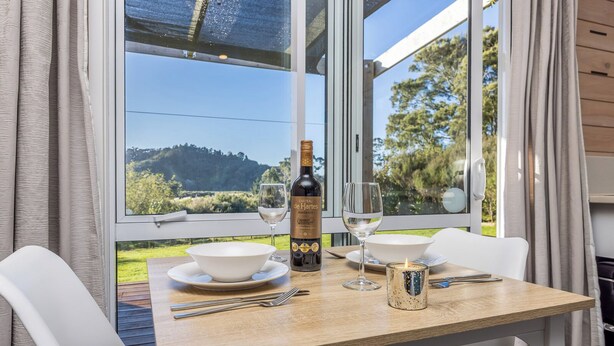 A dining table with a bottle of wine, two glasses, a candle, and cutlery.