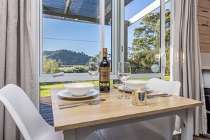A dining table with a bottle of wine, two glasses, a candle, and cutlery. - Manuka Views - Close to Thermal Hot Pools (Kaukapakapa)