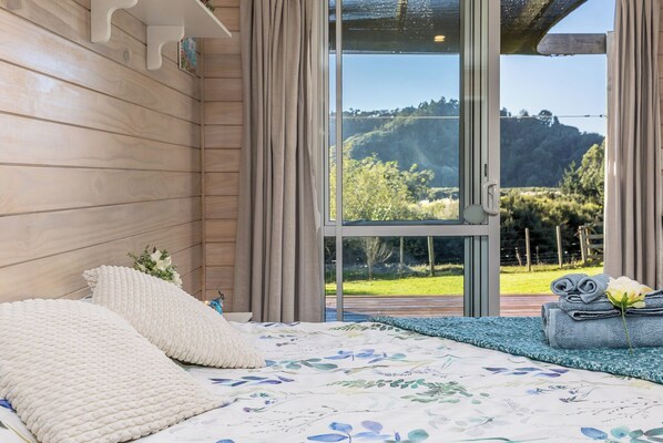 Un dormitorio con un ventanal grande, una cama con ropa de cama floral y vistas a un paisaje verde.