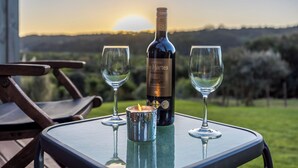 A bottle of Chateau de Hartenstein wine, two glasses, and a candle on a table with a view of a sunset and hills.