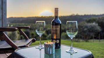 Una botella de vino Chateau de Hartenstein, dos copas y una vela sobre una mesa con vistas a un atardecer y colinas.